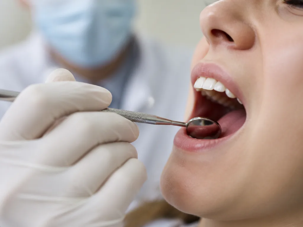 Tandläkare undersöker en patients tandkött med en dentalspegel vid en tandläkarkontroll